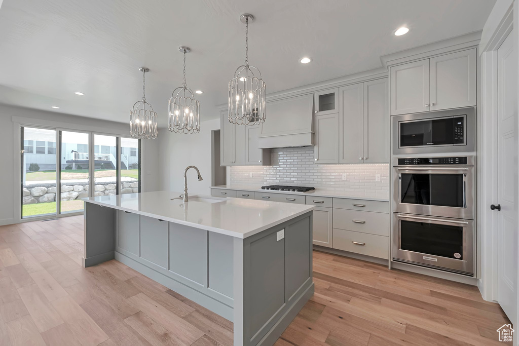 Kitchen featuring premium range hood, light hardwood / wood-style floors, pendant lighting, a center island with sink, and sink