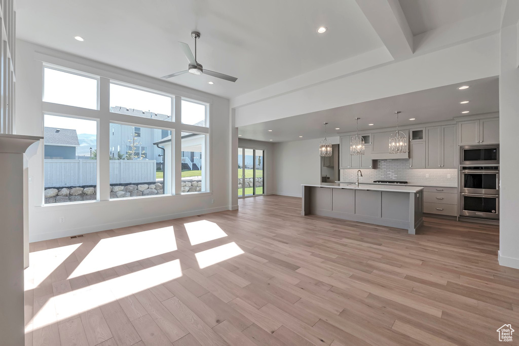 Unfurnished living room with ceiling fan with notable chandelier, light hardwood / wood-style floors, and a healthy amount of sunlight