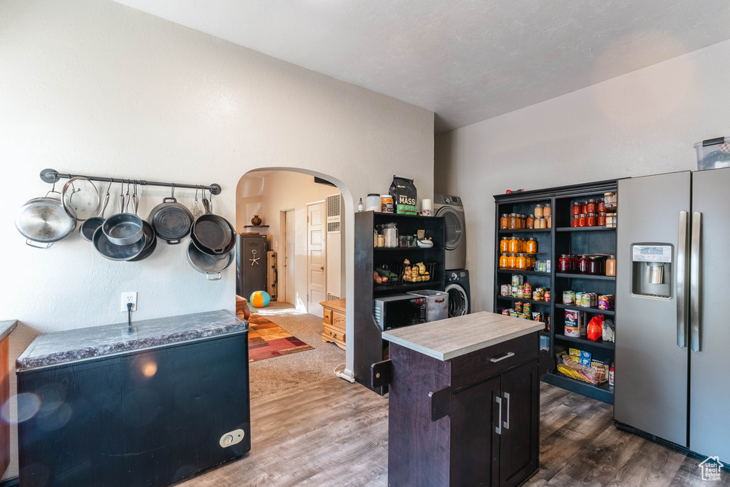 Kitchen featuring dark hardwood / wood-style flooring, stacked washer and dryer, stainless steel fridge with ice dispenser, and a center island