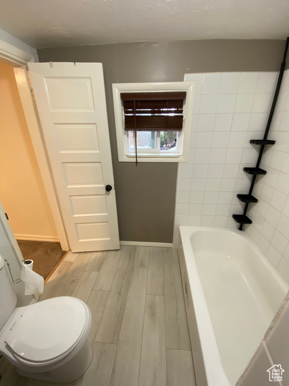 Bathroom featuring hardwood / wood-style floors, a textured ceiling, a washtub, and toilet