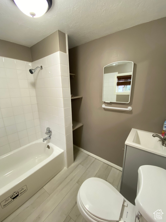 Full bathroom featuring a textured ceiling, hardwood / wood-style flooring, tiled shower / bath combo, vanity, and toilet