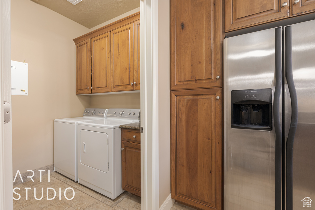 Clothes washing area featuring a textured ceiling, separate washer and dryer, light tile patterned flooring, and cabinets