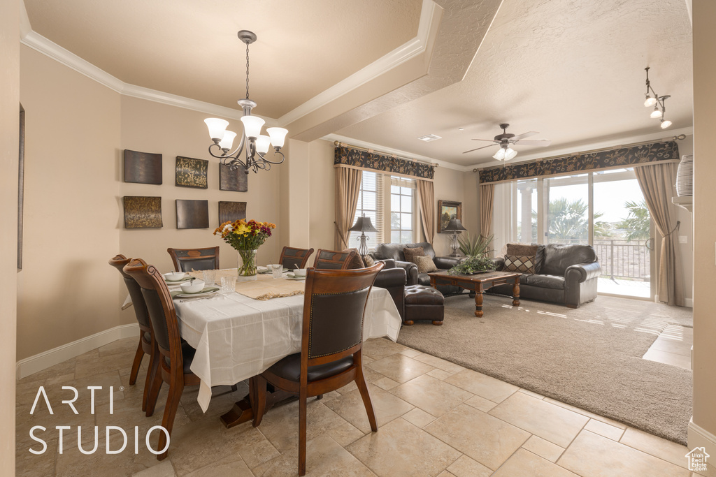 Dining room with ceiling fan with notable chandelier, crown molding, and light colored carpet