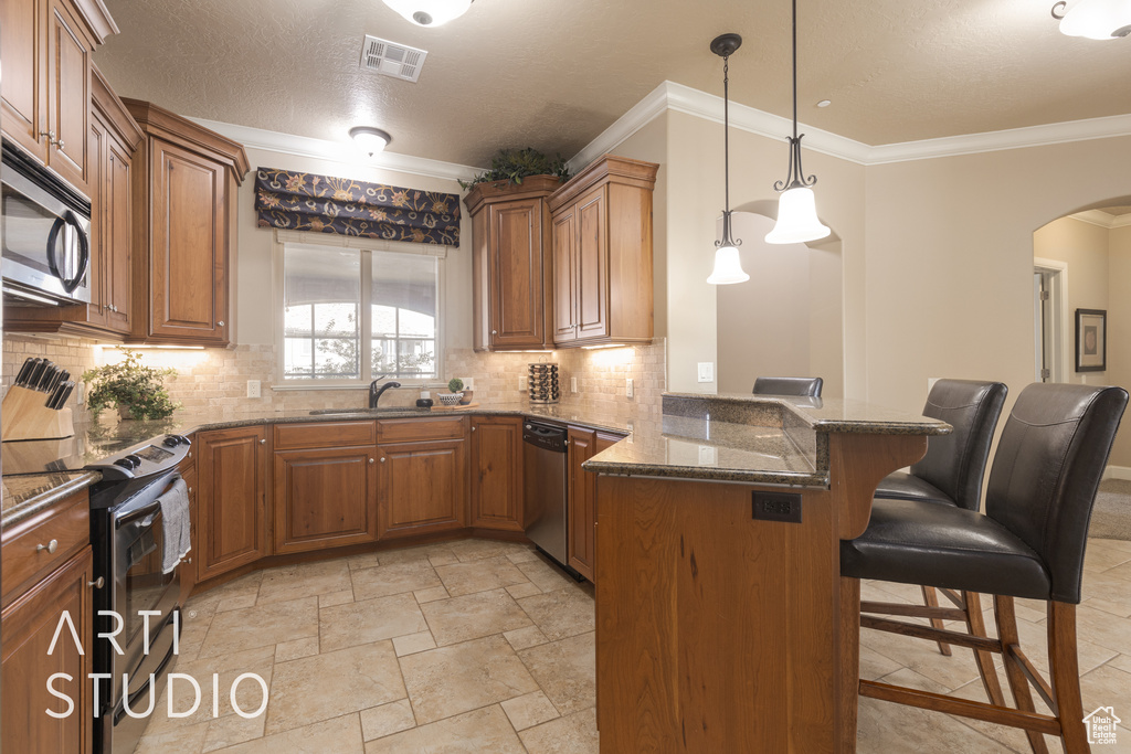 Kitchen with kitchen peninsula, a kitchen breakfast bar, stainless steel appliances, ornamental molding, and dark stone countertops