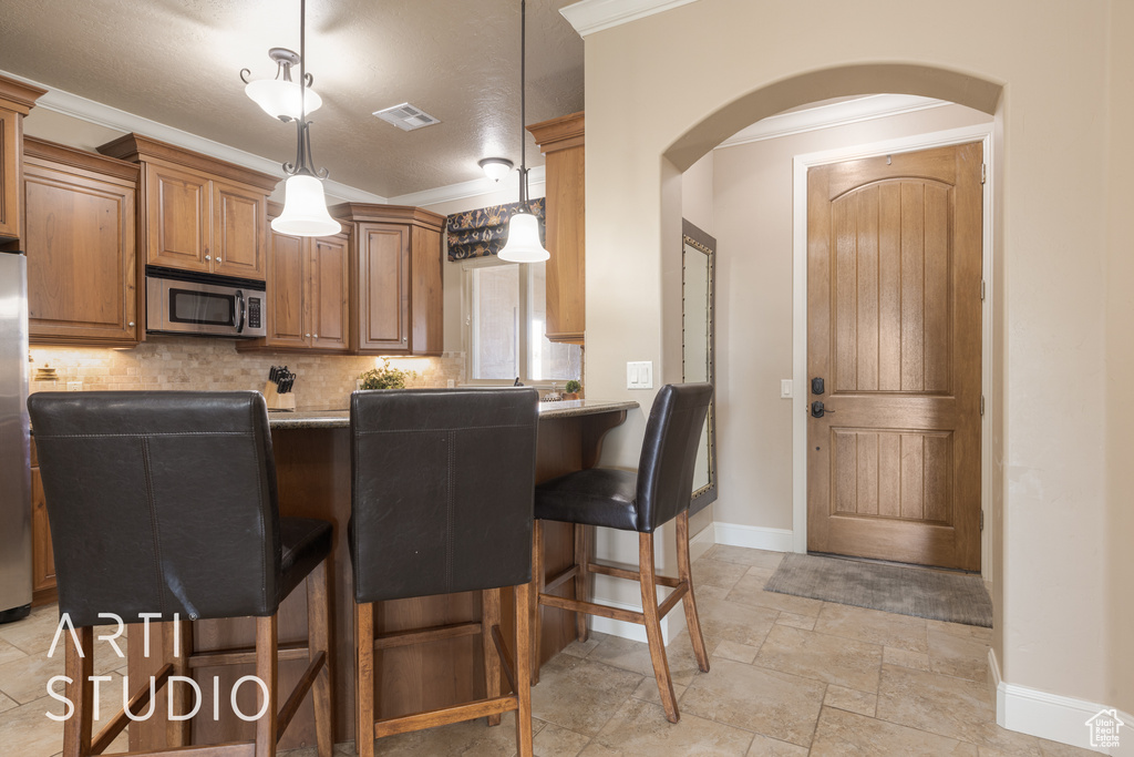 Kitchen featuring pendant lighting, a breakfast bar, kitchen peninsula, decorative backsplash, and appliances with stainless steel finishes