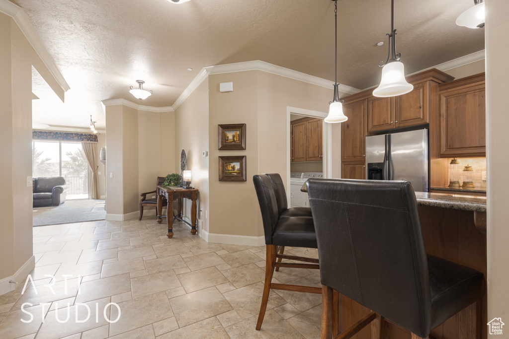 Kitchen with pendant lighting, ornamental molding, backsplash, stainless steel fridge with ice dispenser, and a breakfast bar area