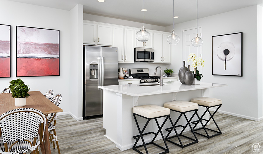 Kitchen featuring white cabinets, an island with sink, pendant lighting, appliances with stainless steel finishes, and light hardwood / wood-style floors