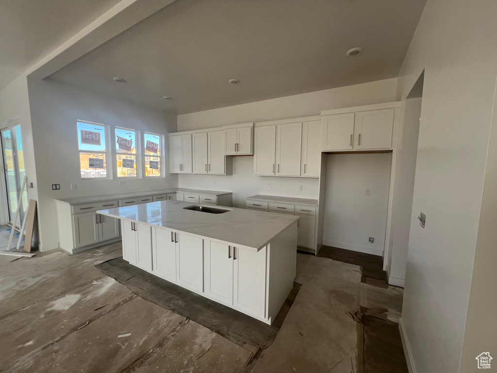 Kitchen with a center island, light stone counters, and white cabinetry