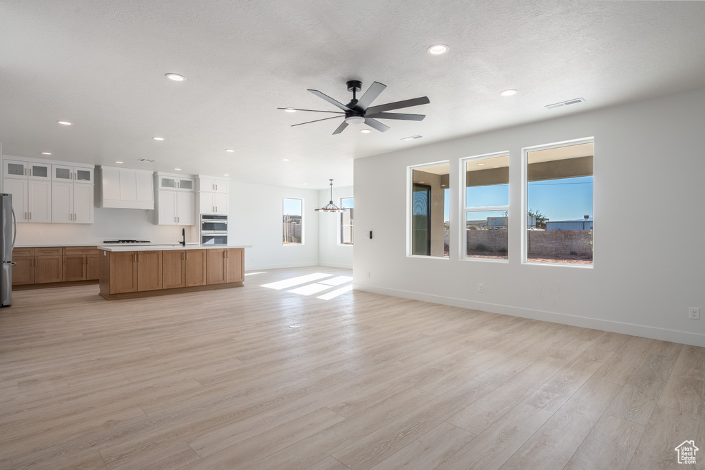 Unfurnished living room featuring ceiling fan with notable chandelier, sink, and light hardwood / wood-style flooring