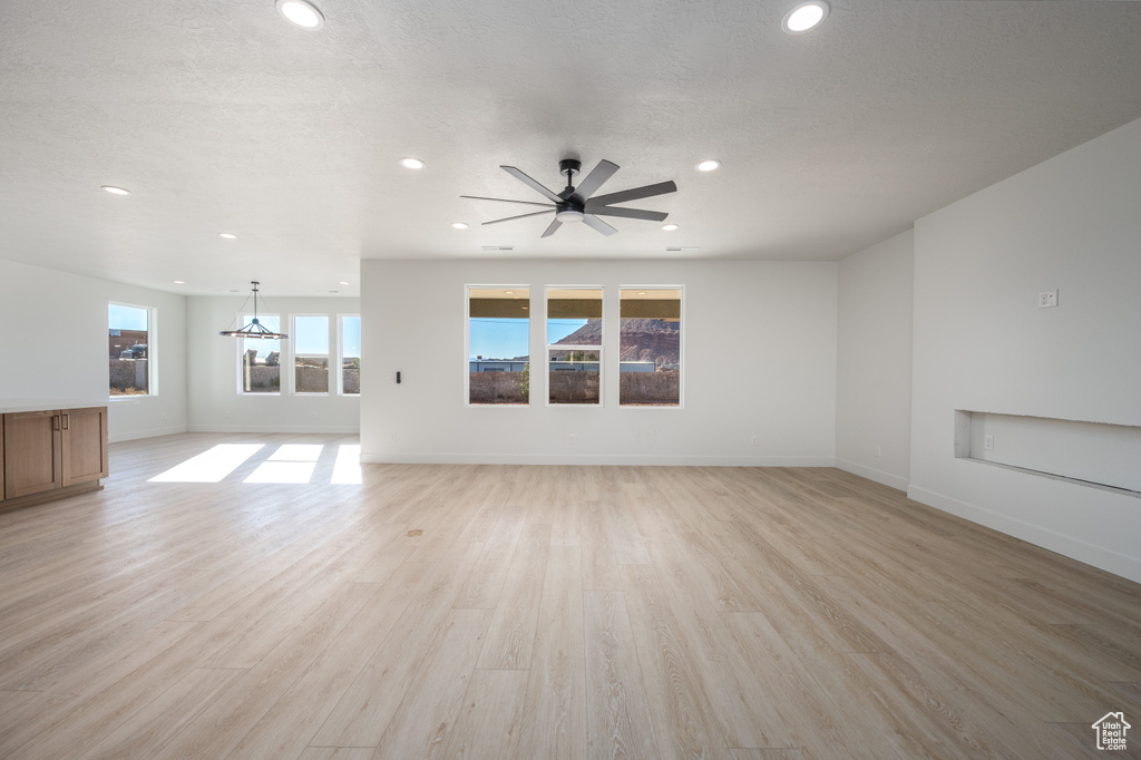 Unfurnished living room featuring ceiling fan with notable chandelier and light hardwood / wood-style flooring