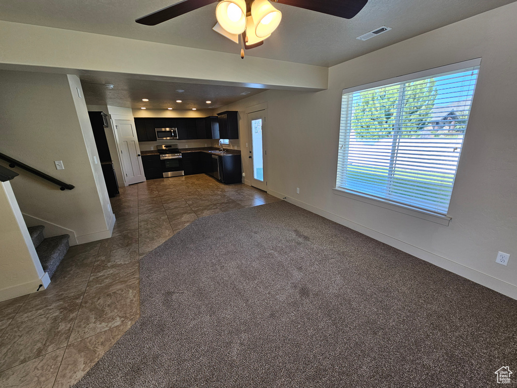 Unfurnished living room featuring dark carpet, sink, and ceiling fan