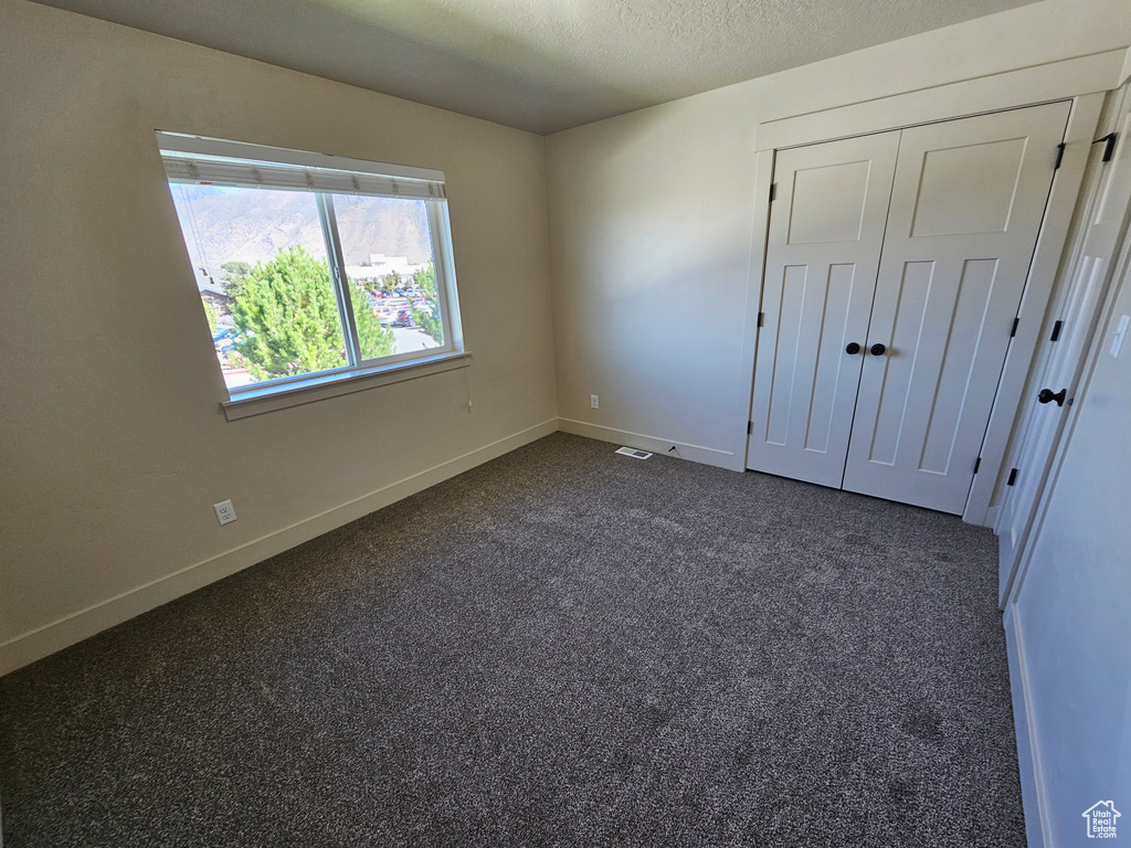 Unfurnished bedroom featuring a textured ceiling, dark colored carpet, and a closet