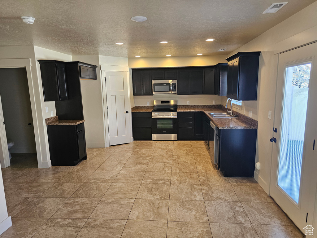 Kitchen featuring stainless steel appliances, dark stone countertops, a textured ceiling, and sink