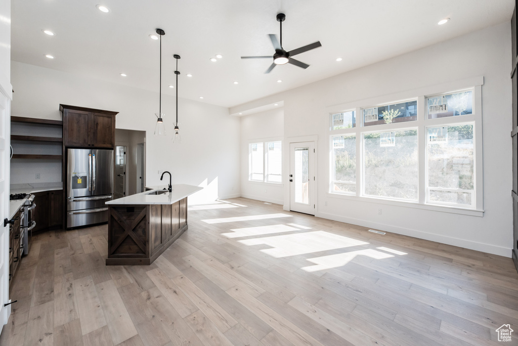 Kitchen with pendant lighting, stainless steel appliances, light hardwood / wood-style floors, and a center island with sink