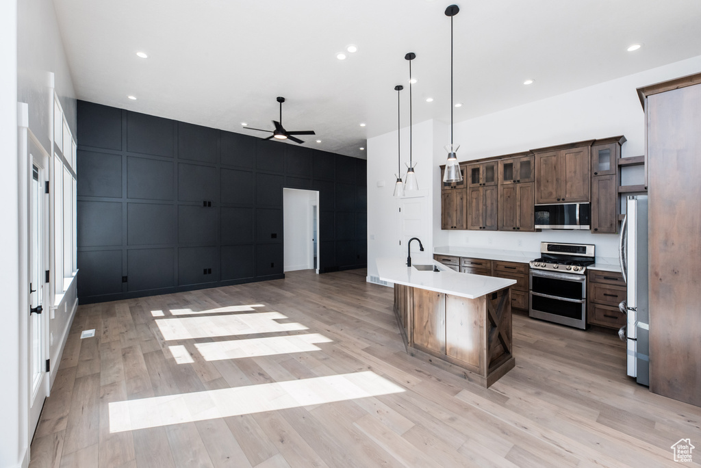 Kitchen featuring pendant lighting, dark brown cabinets, a kitchen island with sink, stainless steel appliances, and light wood-type flooring