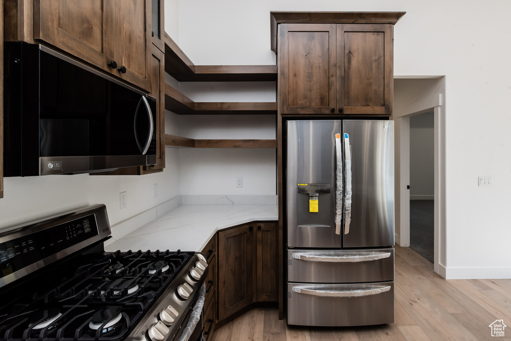 Kitchen featuring dark brown cabinetry, appliances with stainless steel finishes, light wood-type flooring, and light stone counters