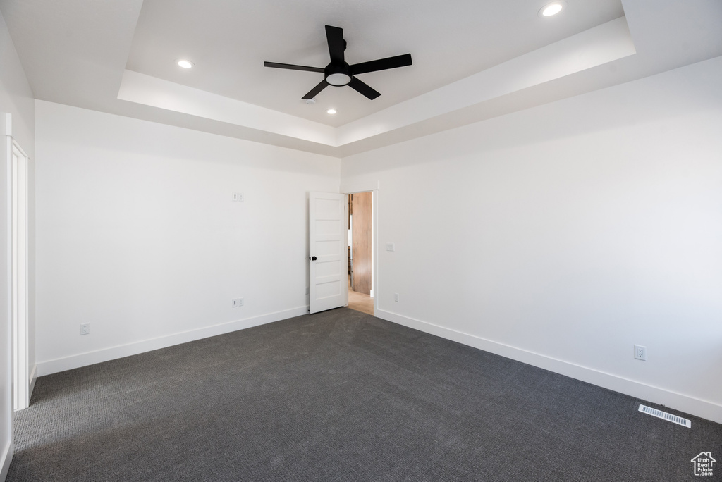 Unfurnished room featuring a tray ceiling, dark colored carpet, and ceiling fan