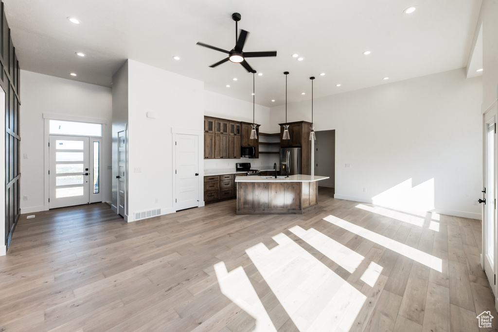 Kitchen with appliances with stainless steel finishes, light hardwood / wood-style floors, a kitchen island, pendant lighting, and dark brown cabinetry