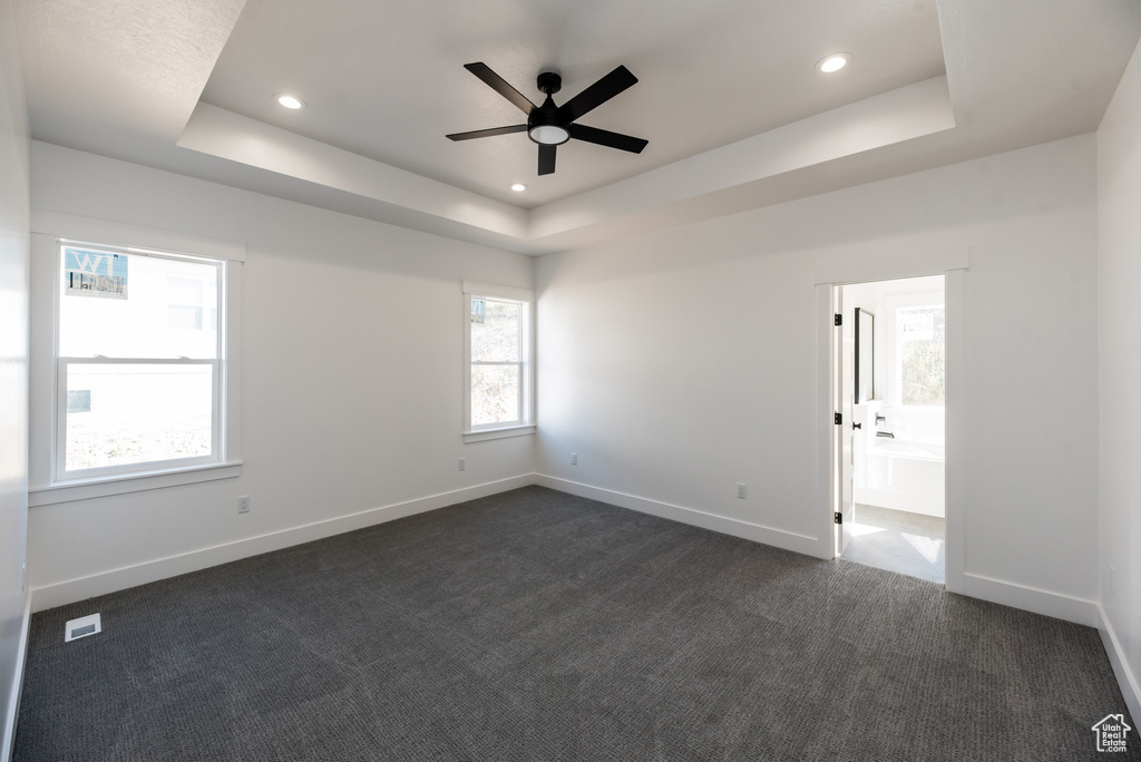 Carpeted spare room with a tray ceiling and ceiling fan