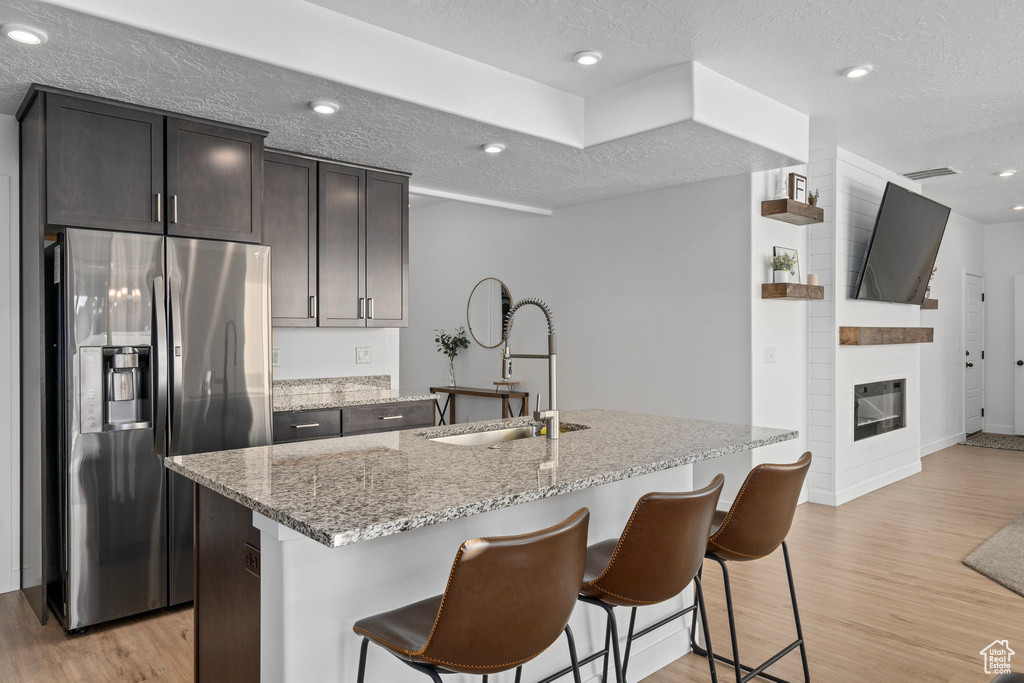 Kitchen featuring an island with sink, sink, a textured ceiling, light hardwood / wood-style flooring, and stainless steel fridge with ice dispenser