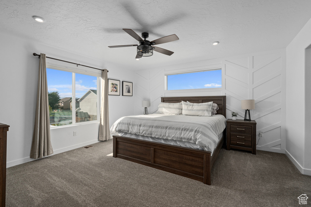 Bedroom with dark carpet, ceiling fan, and a textured ceiling