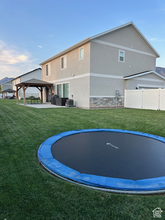 Back of property with a patio, a trampoline, central AC unit, and a yard