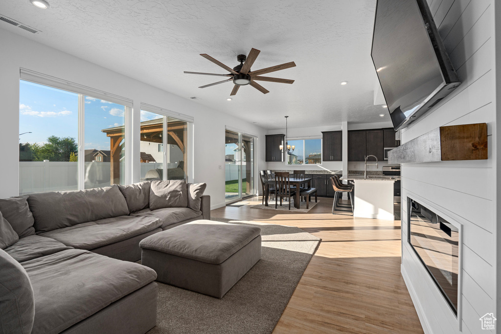 Living room with a textured ceiling, ceiling fan with notable chandelier, and light wood-type flooring