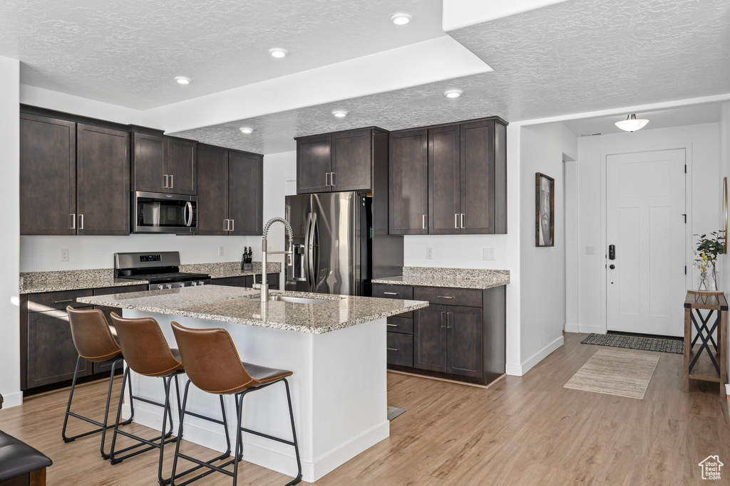 Kitchen featuring light hardwood / wood-style floors, stainless steel appliances, a textured ceiling, a kitchen island with sink, and sink