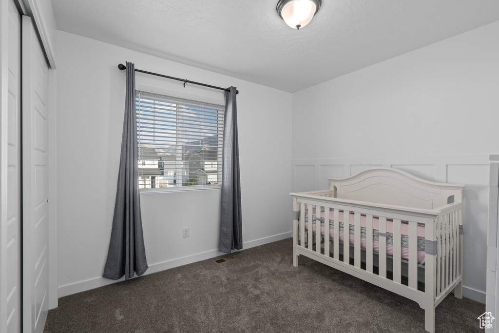 Carpeted bedroom featuring a textured ceiling, a nursery area, and a closet