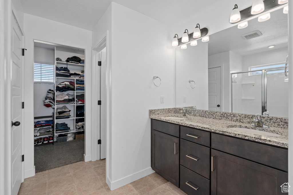 Bathroom with tile patterned floors, vanity, a shower with shower door, and a wealth of natural light