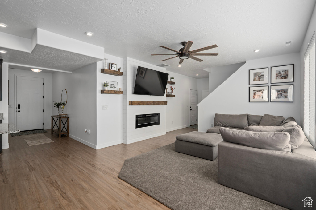 Living room featuring wood-type flooring, a textured ceiling, ceiling fan, and a large fireplace