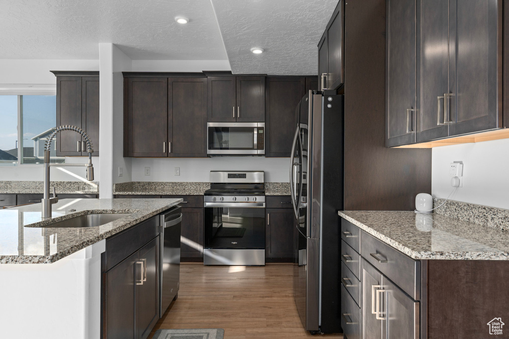 Kitchen featuring a textured ceiling, dark hardwood / wood-style flooring, stainless steel appliances, and light stone counters