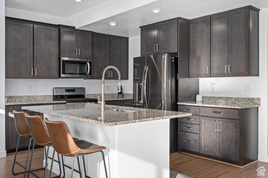 Kitchen with appliances with stainless steel finishes, a textured ceiling, and an island with sink