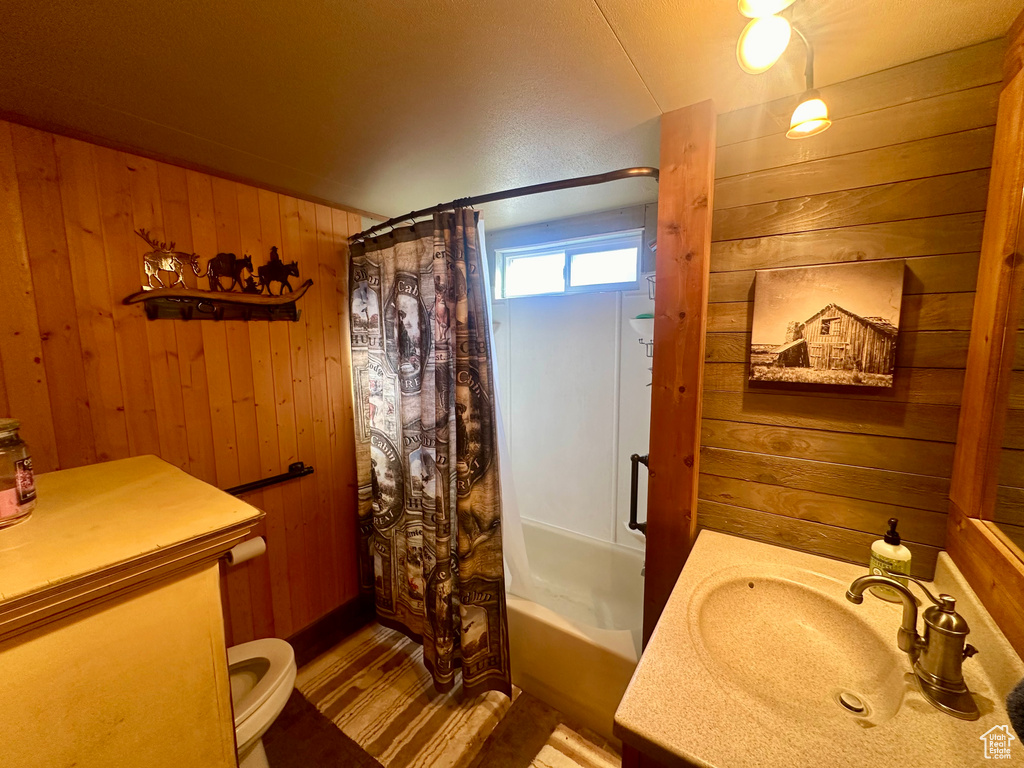 Full bathroom with wooden walls, vanity, shower / tub combo, and toilet