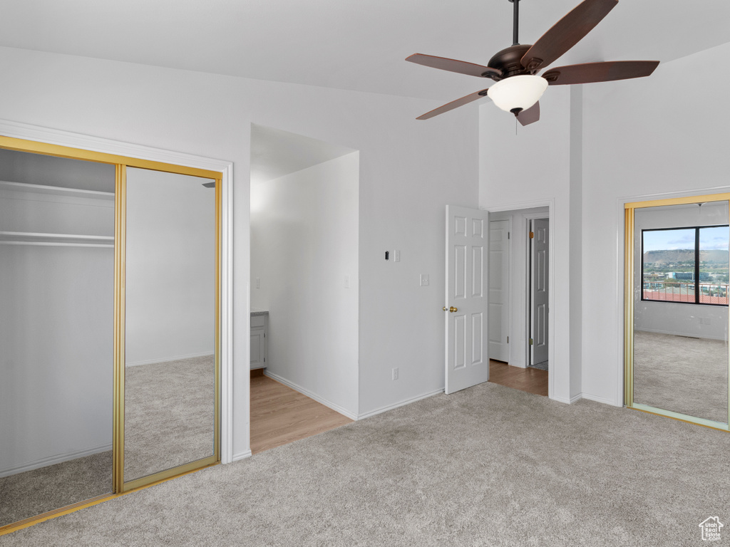 Unfurnished bedroom with high vaulted ceiling, multiple closets, ceiling fan, and light colored carpet