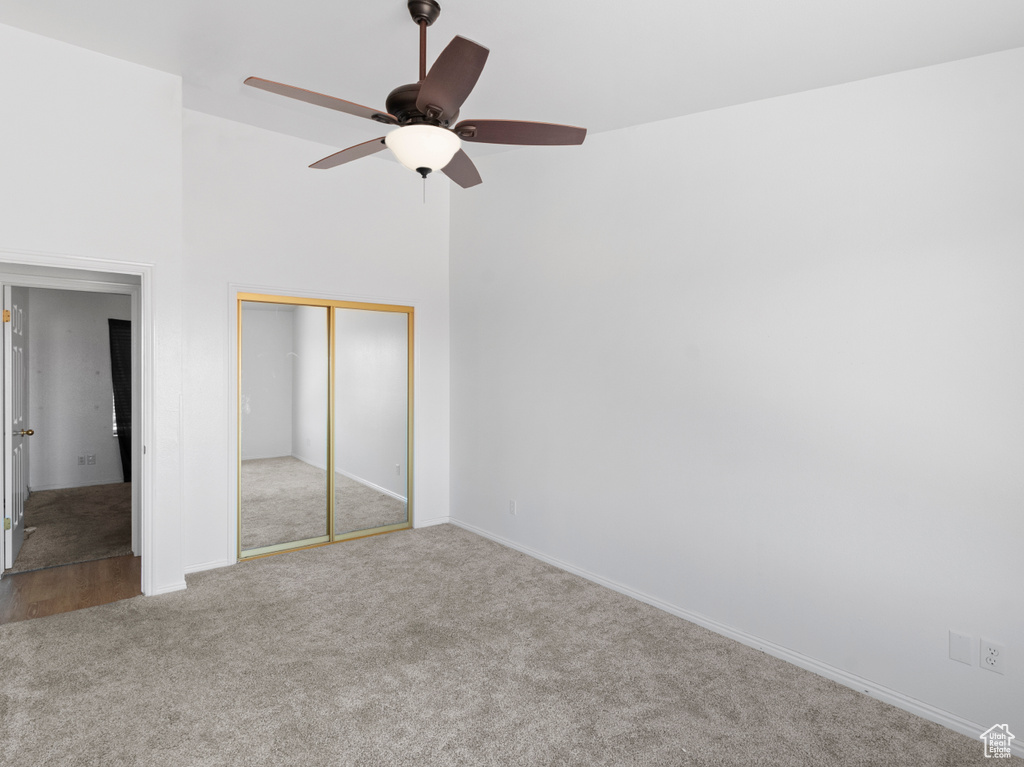 Unfurnished bedroom featuring ceiling fan, a closet, light carpet, and a towering ceiling