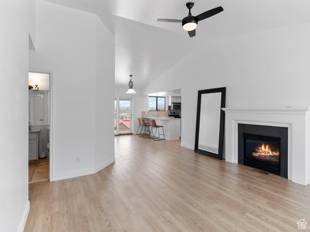 Unfurnished living room with ceiling fan, light wood-type flooring, and high vaulted ceiling