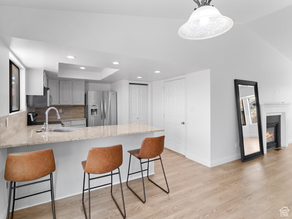 Kitchen featuring stainless steel fridge, sink, kitchen peninsula, gray cabinetry, and decorative light fixtures