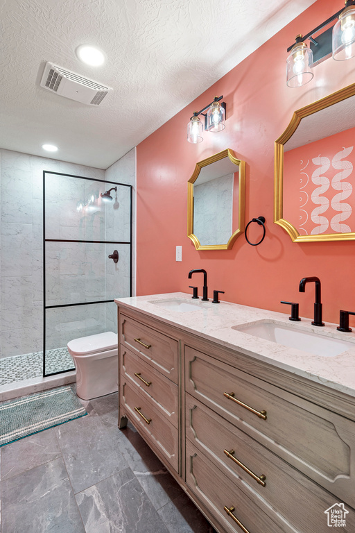 Bathroom featuring tiled shower, a textured ceiling, vanity, and toilet