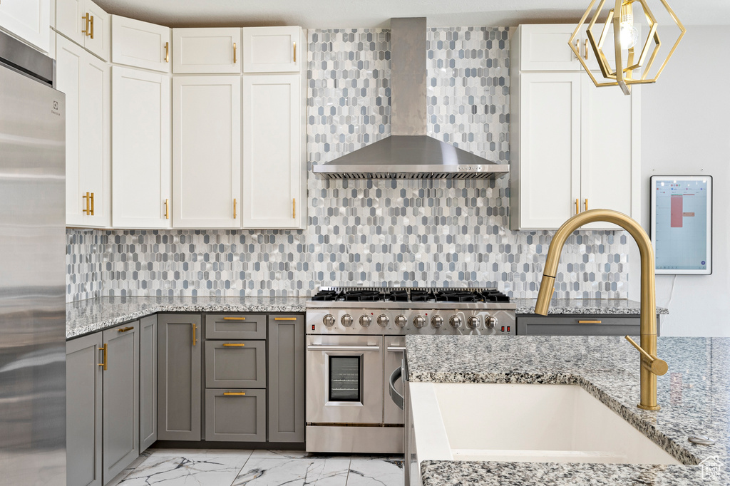 Kitchen featuring gray cabinets, white cabinetry, wall chimney range hood, appliances with stainless steel finishes, and decorative light fixtures