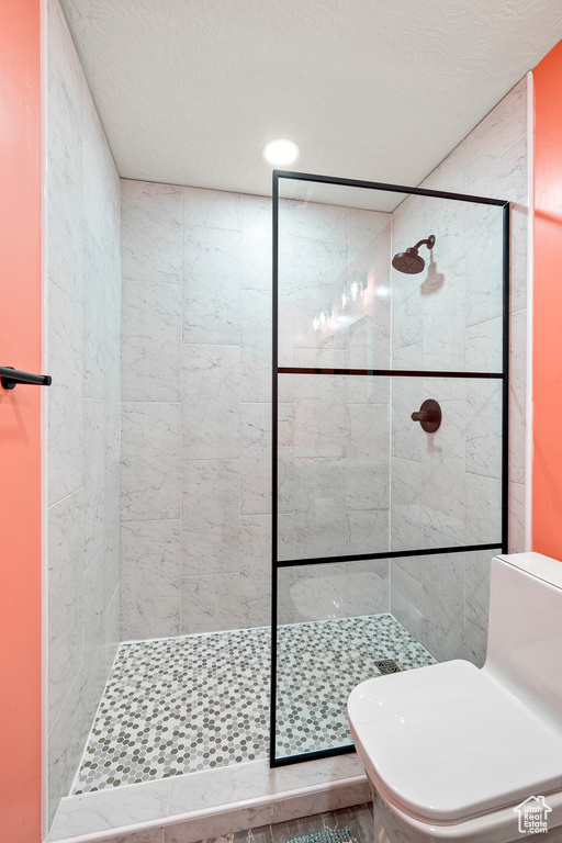 Bathroom with toilet, tile patterned floors, and tiled shower