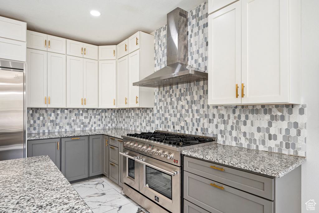 Kitchen featuring tasteful backsplash, high end appliances, wall chimney range hood, and gray cabinetry