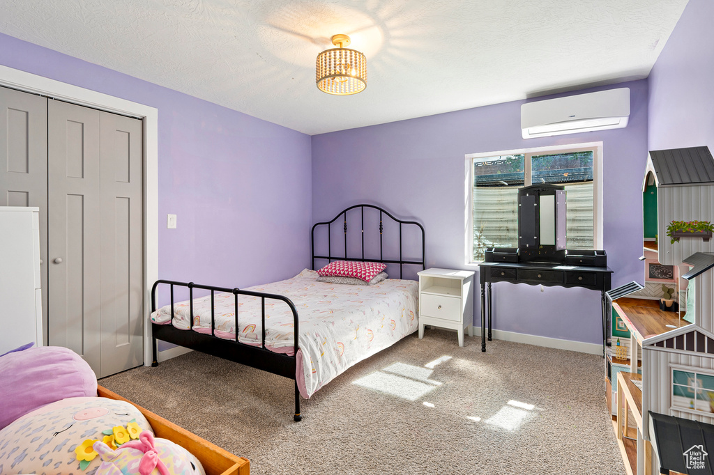 Carpeted bedroom with a textured ceiling, a wall mounted air conditioner, and a closet