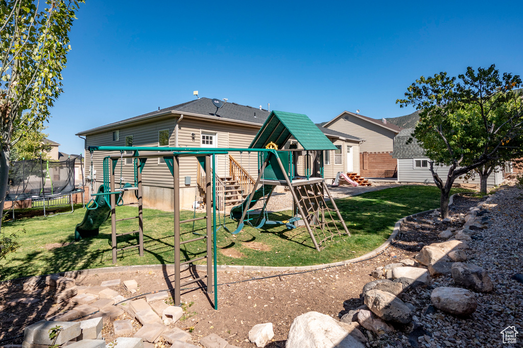 Rear view of house with a playground, a trampoline, and a lawn