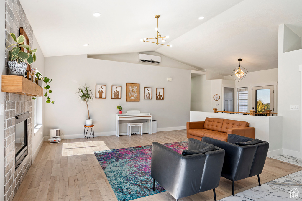 Living room with an inviting chandelier, lofted ceiling, an AC wall unit, and light hardwood / wood-style flooring