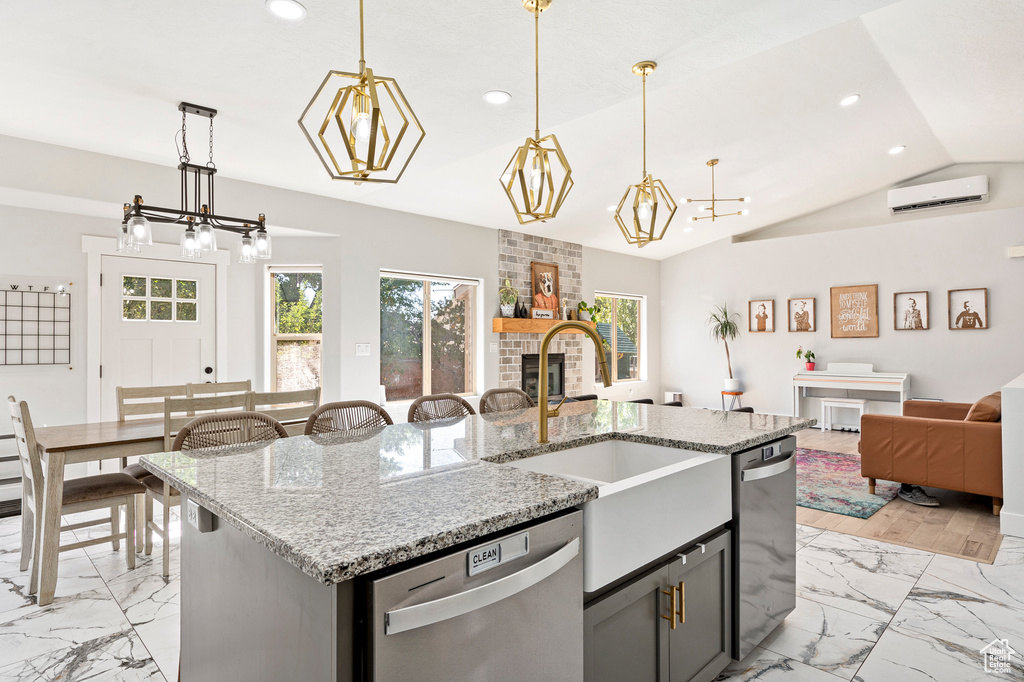 Kitchen with vaulted ceiling, a fireplace, stainless steel dishwasher, a kitchen island with sink, and sink