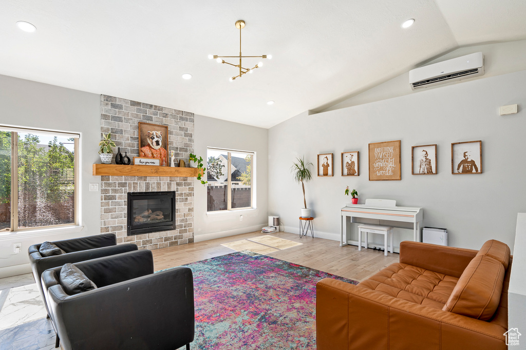 Living room featuring a wall mounted air conditioner, hardwood / wood-style flooring, a notable chandelier, a fireplace, and vaulted ceiling