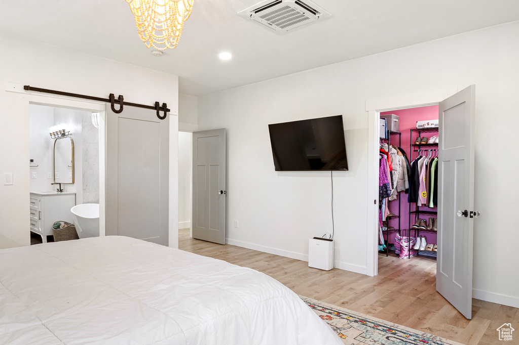 Bedroom with a spacious closet, a barn door, a closet, light wood-type flooring, and ensuite bath