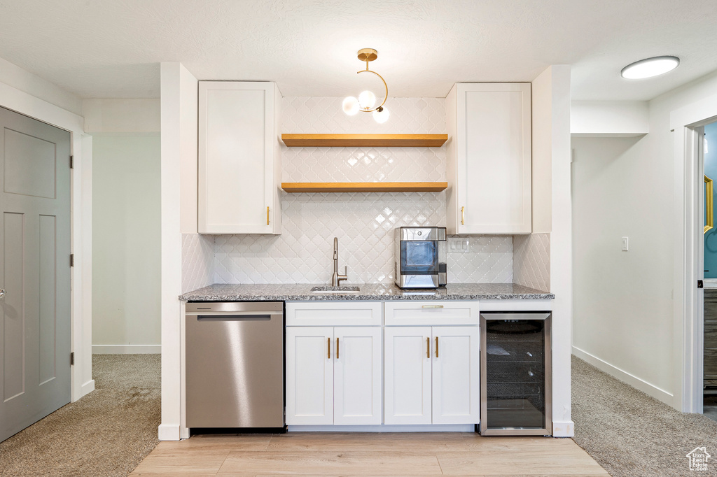 Kitchen with light stone counters, wine cooler, white cabinets, dishwasher, and sink