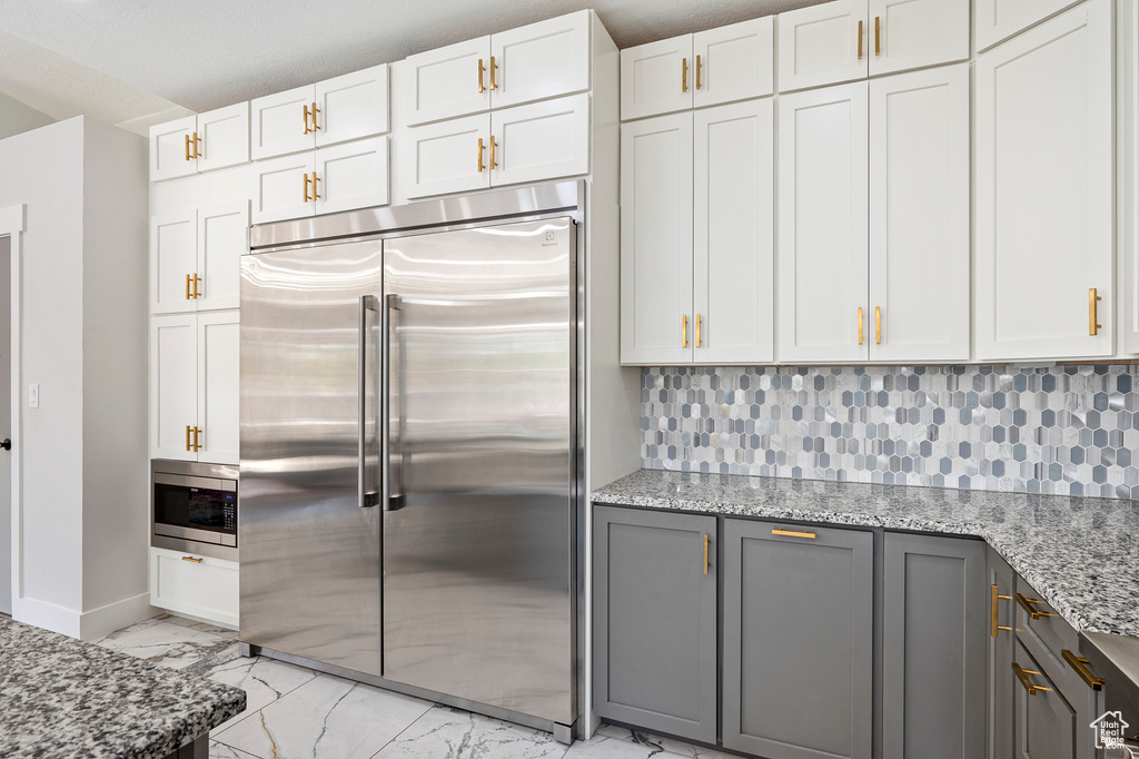 Kitchen with gray cabinetry, stainless steel appliances, white cabinetry, and light stone countertops